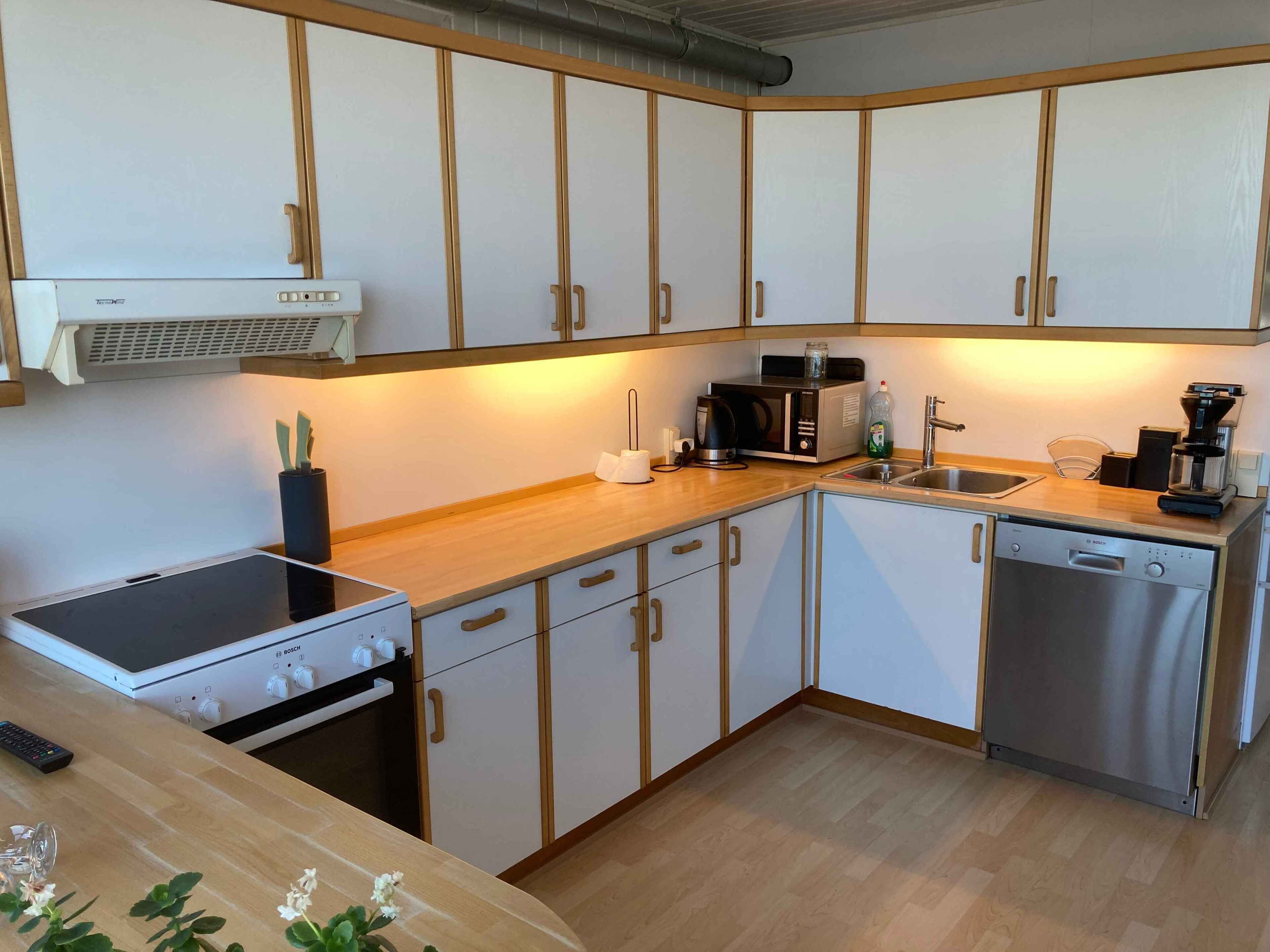 A compact kitchen with white cabinets, a Bosch dishwasher, a microwave, and a coffee maker.