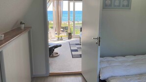 Ein Zimmer mit Bett, einem an der Wand befestigten Fernseher und einem Balkon mit Meerblick.