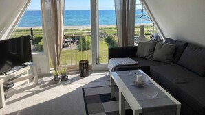 Ein Balkon mit Fernseher, Sofa und Tisch, mit Blick auf Strand und Meer.