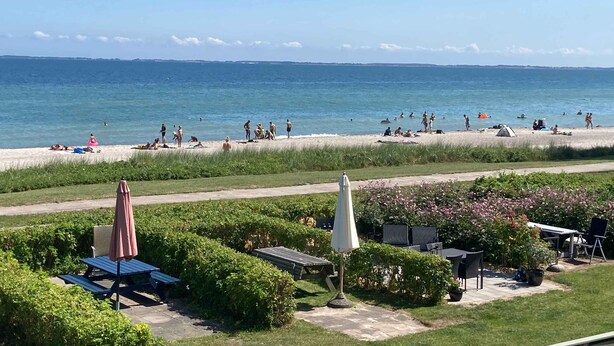 Ein Strand mit badenden Menschen, Sonnenschirmen und Liegestühlen, sowie einem Zelt.