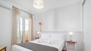 Une chambre d’hôtel avec un lit, deux tables de chevet avec des lampes, une fenêtre avec des rideaux et une fleur accrochée au mur.