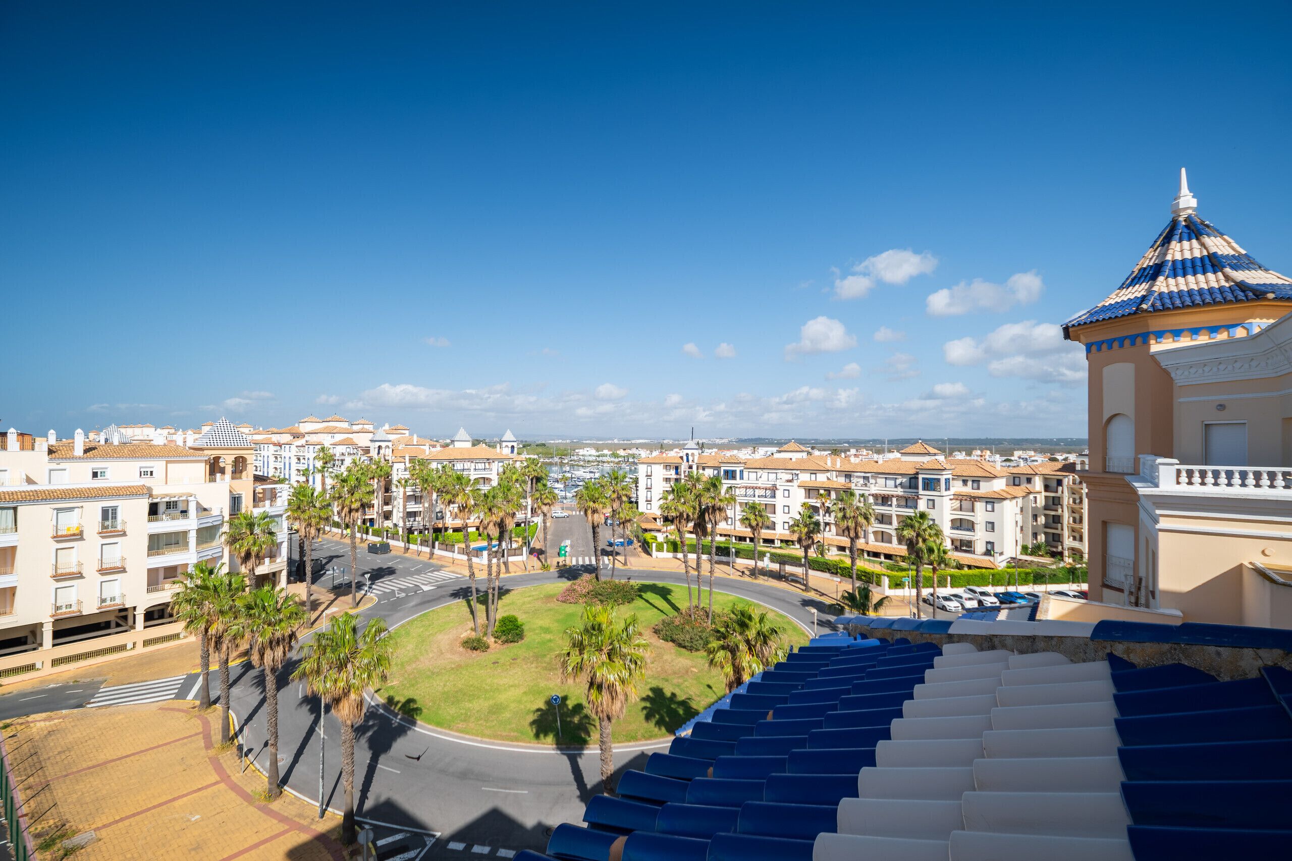 A coastal hotel with a central courtyard, palm trees, and a view of the sea.