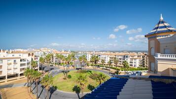 A coastal hotel with a central courtyard, palm trees, and a view of the sea.