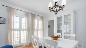 Un coin repas avec une table blanche, des chaises bleues, un lustre et un buffet aux portes vitrées.