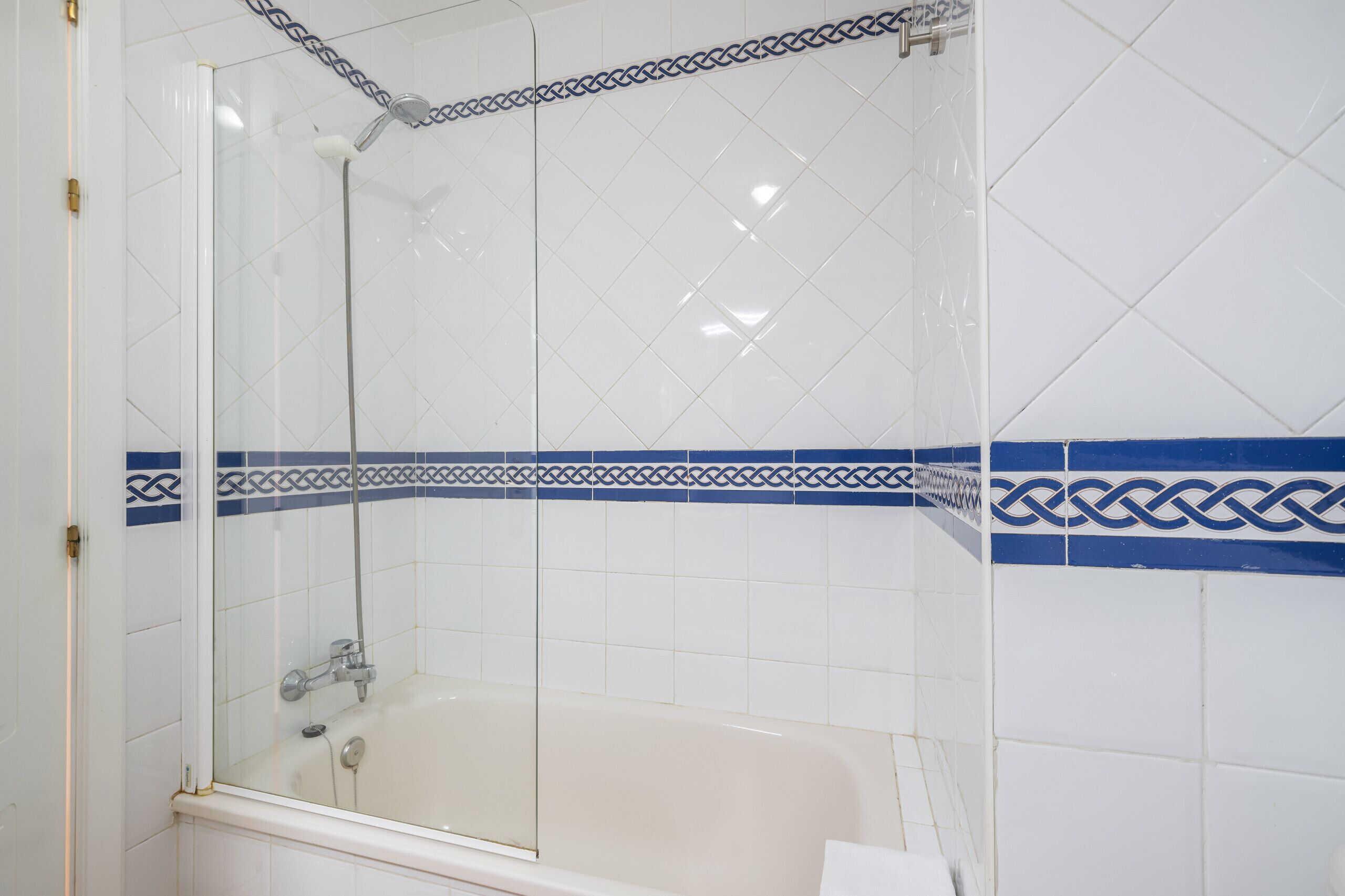 Een badkamer met een douchecabine, een bad en witte betegelde wanden met blauwe decoratieranden.