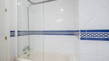 Een badkamer met een douchecabine, een bad en witte betegelde wanden met blauwe decoratieranden.