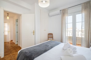 A hotel room with a bed, a chair, a balcony with a view, and an air conditioning unit.