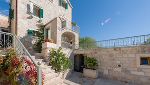 A stone building with a balcony, a staircase, and a view of the sea. - Villa Brač Stone with Swimming Pool (Bol)