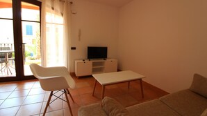 Ein Wohnzimmer mit einer Couch, einem weißen Sessel, einem kleinen Tisch und einem Fernseher auf einem weißen Schrank.