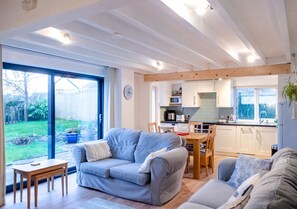 Relax in a spacious living room with a garden view, featuring a sofa, dining table, and kitchen area.