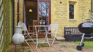 An outdoor patio with a table and chairs, a barbecue grill, and a large urn. - Stepping Stones Cottage - sleeps 4 guests  in 2 bedrooms (Blockley)