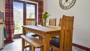 A wooden dining table with benches, a vase with flowers, and a clock on the wall. - Stepping Stones Cottage - sleeps 4 guests  in 2 bedrooms (Blockley)