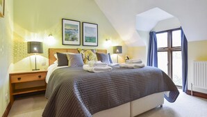 A bedroom with a large bed, two bedside lamps, a window with curtains, and two framed pictures on the wall. - Stepping Stones Cottage - sleeps 4 guests  in 2 bedrooms (Blockley)