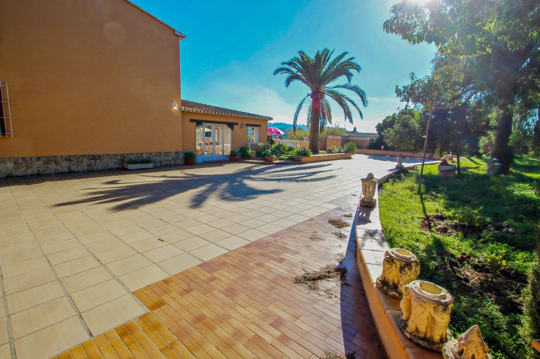 A spacious outdoor area with a paved walkway, a building with a tiled roof, and a palm tree.