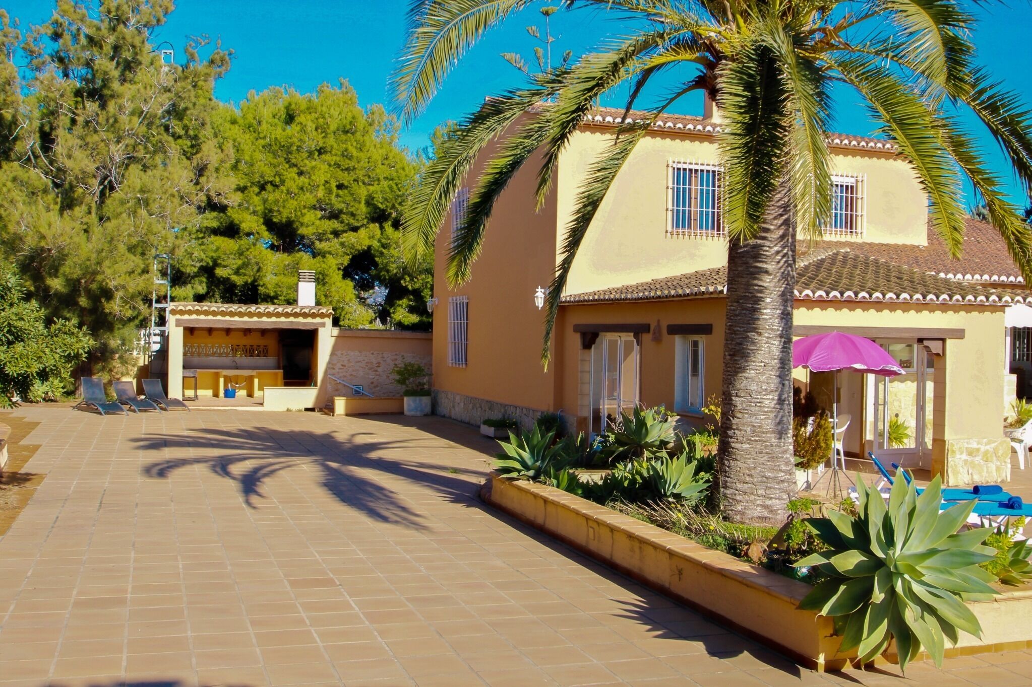 A two-story building with a tiled patio, palm trees, and outdoor seating.