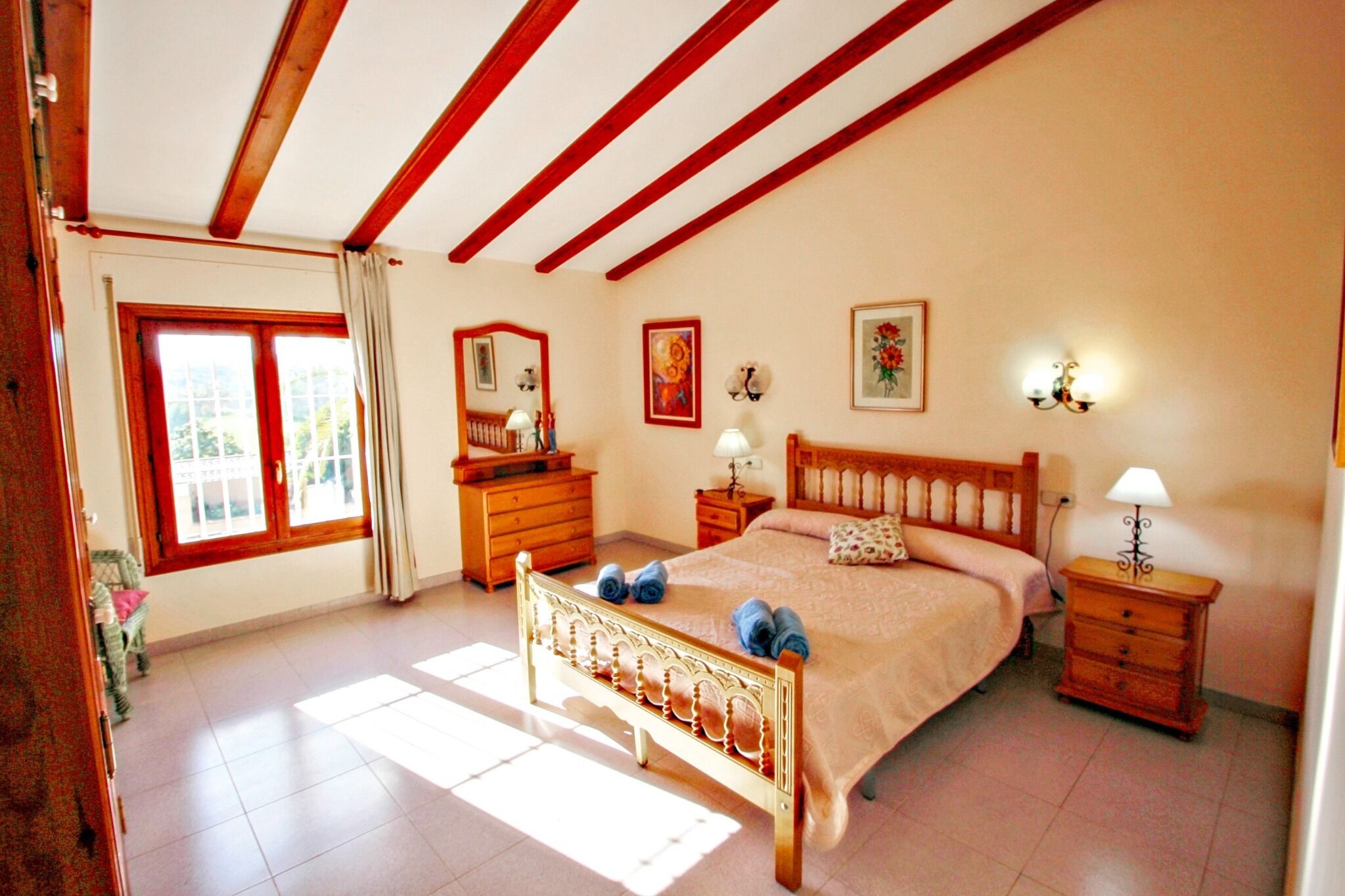 A bedroom with a wooden bed, a nightstand, a dresser, a window with curtains, and a painting on the wall.