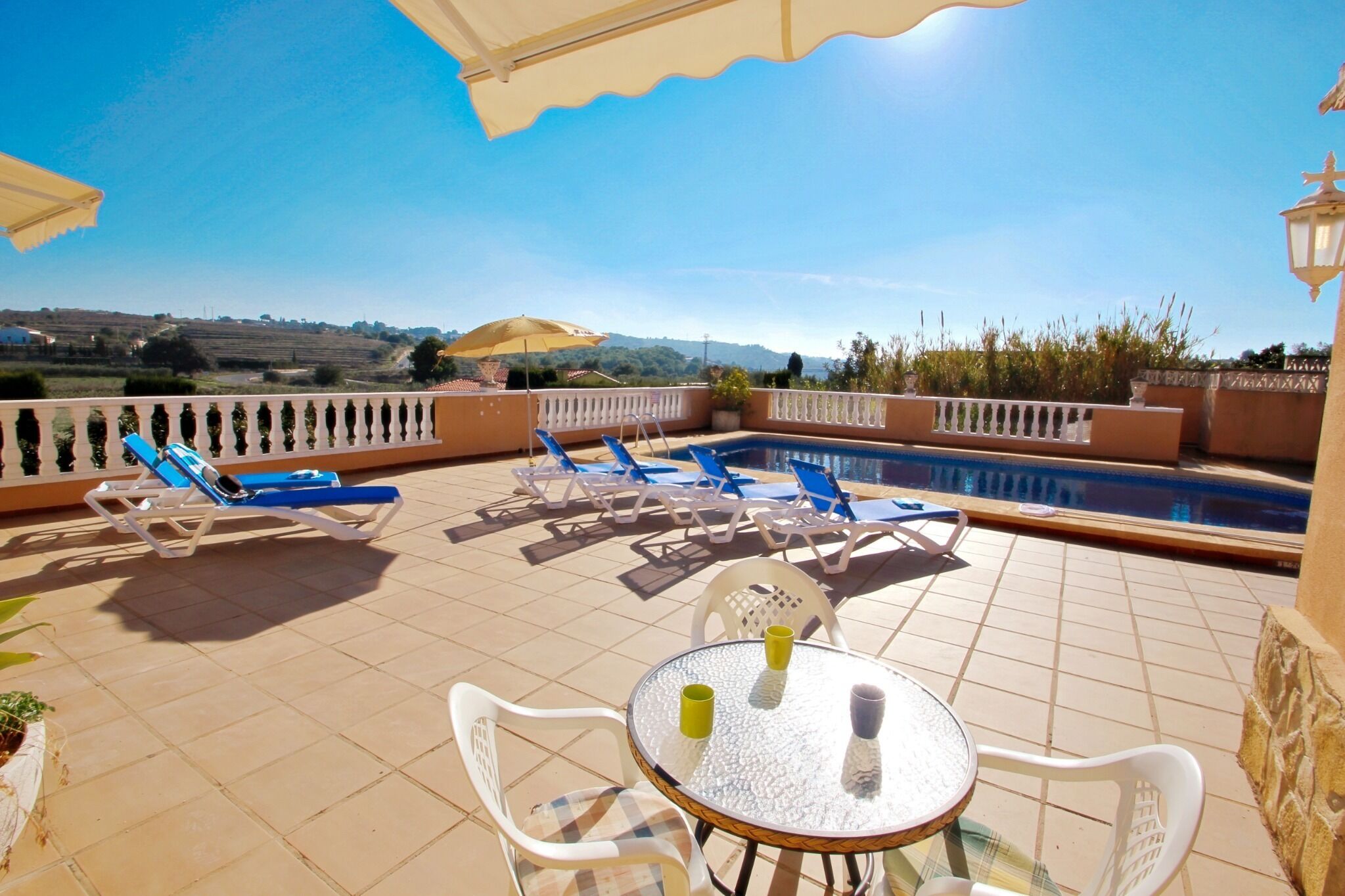 A poolside area with lounge chairs, a table, and a view of the countryside.