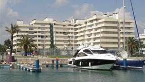 A marina with a white yacht docked in the foreground and a multi-story building in the background. - Luxury apartment in private condominium, with pool (Quarteira)