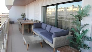 A balcony with a sofa, a table, and chairs, a potted plant, and a view of buildings. - Luxury apartment in private condominium, with pool (Quarteira)