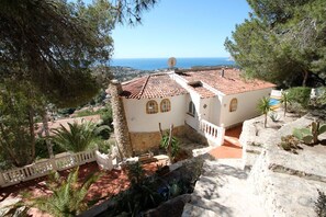 Eine mediterrane Villa mit Terrakotta-Dachziegeln, einer Steintreppe und Blick aufs Meer.