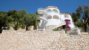 Un edificio a più piani di colore bianco con balconi, circondato da un muro in pietra e alberi.