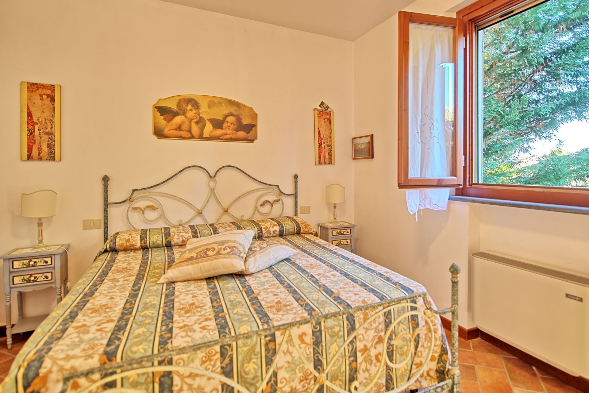 A bedroom with a bed, two bedside tables, a window, and a wall with artwork.