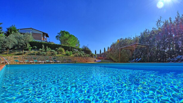 Ein klares, blaues Schwimmbecken mit Liegestühlen und einer Steinmauer im Hintergrund.