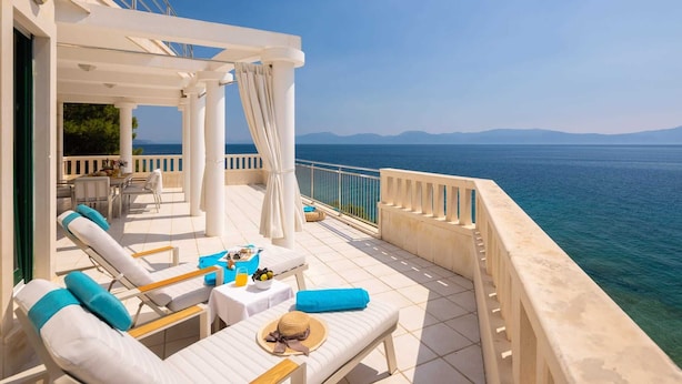 A sunlit outdoor seating area with lounge chairs and tables, overlooking a calm sea and distant mountains. - Beachfront Villa Shades of Summer (Podaca)