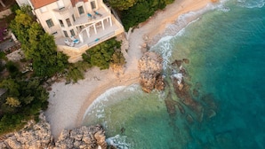 An aerial view of a coastal property with a large house, a sandy beach, and rocky cliffs. - Beachfront Villa Shades of Summer (Podaca)