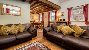 A spacious living room with two leather sofas, a patterned rug, and wooden beams on the ceiling. - The Stables - at Broadgate Farm Cottages (Beverley)