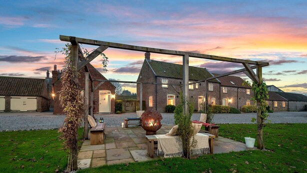 A rustic outdoor seating area with a pergola, stone benches, and a fire pit. - The Stables - at Broadgate Farm Cottages (Beverley)