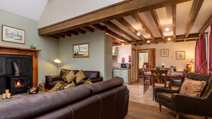 A cozy living room with a fireplace, leather sofa, and wooden beams on the ceiling. - The Stables - at Broadgate Farm Cottages (Beverley)