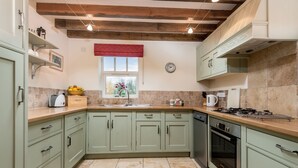A kitchen with light green cabinets, a wooden ceiling, a window with a red valance, and a Bosch oven. - The Stables - at Broadgate Farm Cottages (Beverley)