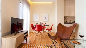 Een moderne woonkamer met een flatscreen-tv, rode stoelen, een glazen salontafel en een eethoek met een tafel gedekt voor twee personen.