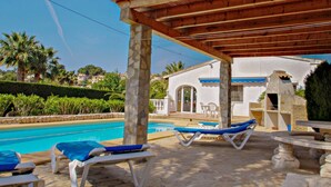A pool area with lounge chairs, a pergola, and a stone building with a tiled roof. - Kathrin - beautiful little house in pretty grounds with lovely views in Benissa (Benissa)