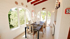 A dining area with a large table and chairs, large arched windows, and a clock on the wall. - Kathrin - beautiful little house in pretty grounds with lovely views in Benissa (Benissa)