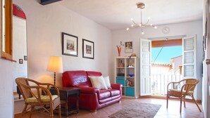 A living room with a red leather sofa, wicker chairs, a small table, a lamp, and a bookshelf.