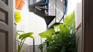A narrow outdoor corridor with a spiral staircase, potted plants, and a tiled floor.