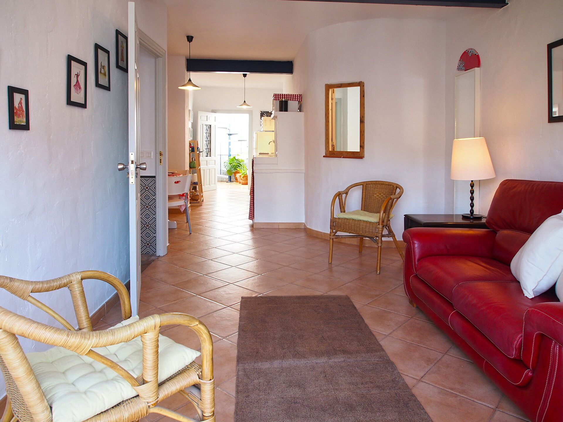 Un salon avec un canapé rouge, des fauteuils en osier, un tapis marron et un coin repas comprenant une table et des chaises.