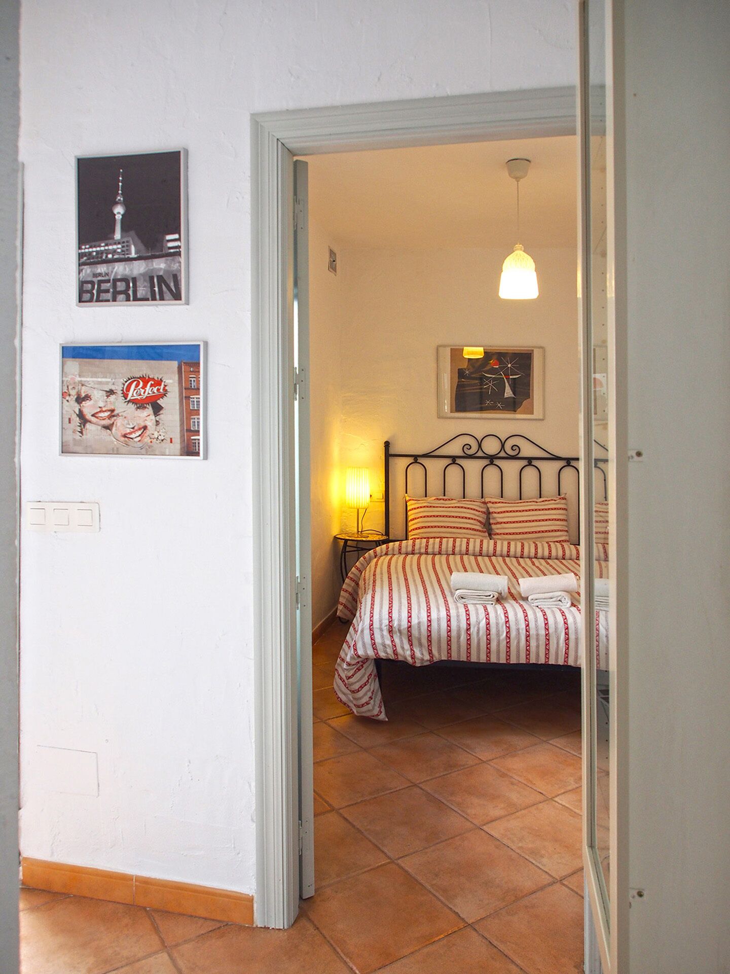 Ein Schlafzimmer mit Bett, Nachttisch, Lampe und Wandkunst, darunter eine Stadtansicht und ein Poster.
