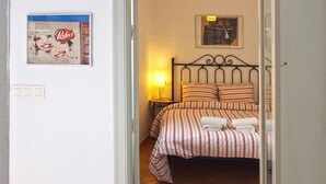 A bedroom with a bed, a nightstand, a lamp, and wall art including a cityscape and a poster.