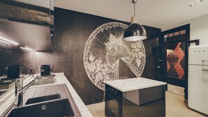A modern kitchen with a central island, stainless steel appliances, and a decorative wall piece. - Master Deco Gem in Bica (Lisboa)