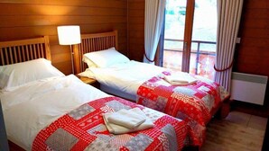 A hotel room with two beds, a nightstand, a lamp, and a view of the outdoors.