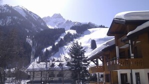 A mountain lodge with wooden balconies and snow-covered roofs, surrounded by snow-covered mountains and pine trees.