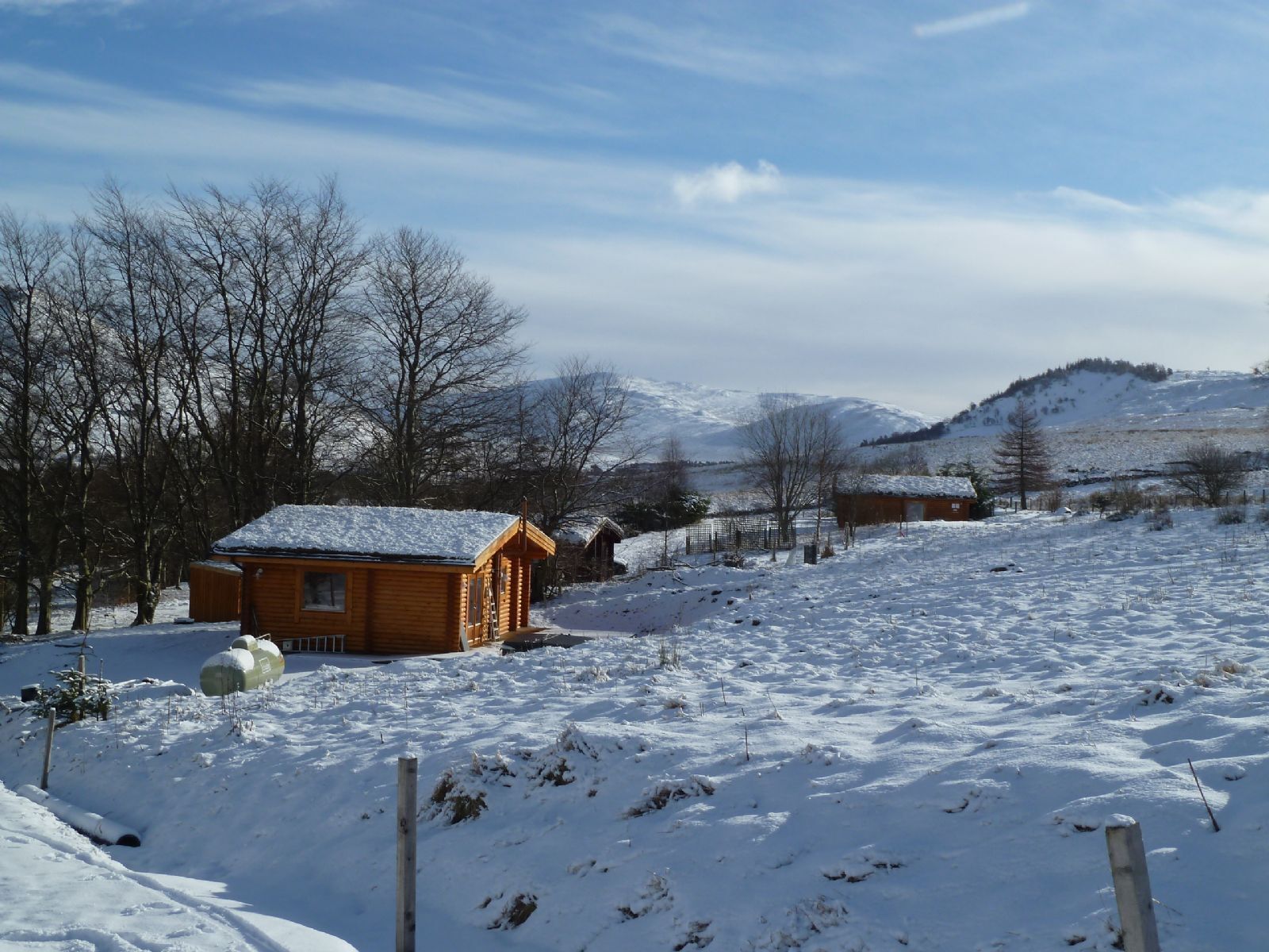 Une cabane en bois, dont le toit est recouvert de neige, entourée d’un paysage enneigé et d’arbres.