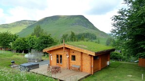 Eine Holzhütte mit Gründach, einer Terrasse mit Gartenmöbeln und einer Bergkulisse.