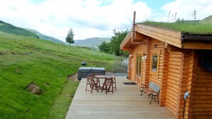 Eine Blockhütte mit einer Terrasse, Sitzgelegenheiten im Freien und einem Whirlpool.