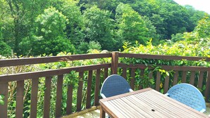 Eine Holzterrasse mit Tisch und Stühlen, mit Blick auf einen dichten Wald.