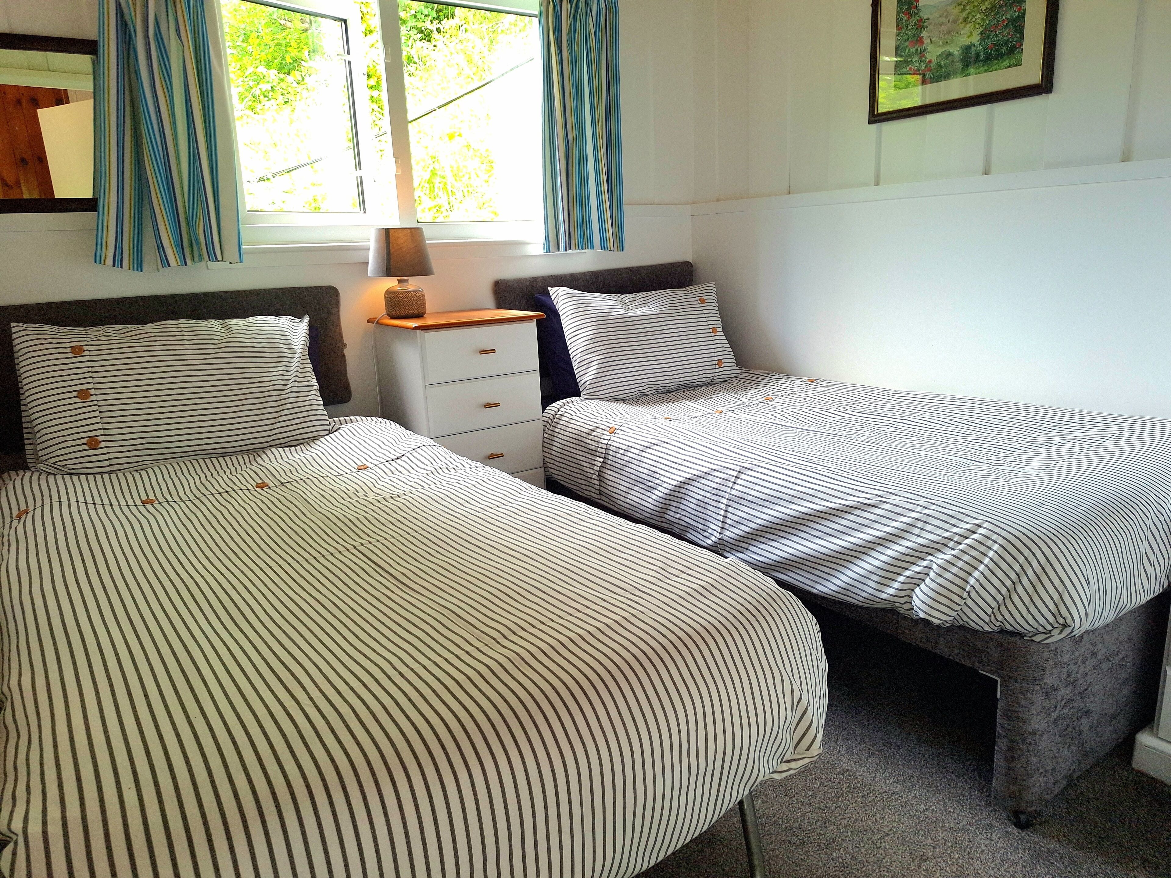 A bedroom with two single beds, a nightstand with a lamp, and a window with curtains.