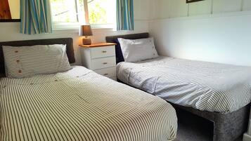 A bedroom with two single beds, a nightstand with a lamp, and a window with curtains.